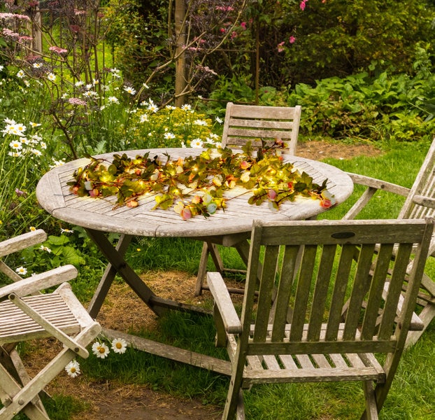Gartenszene mit Holztisch, Stühlen und Lichterkette