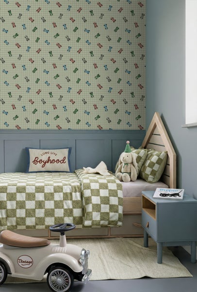 Helles Kinderzimmer mit Tapete mit Rennwagenmotiv, Hausbett aus Holz, karierter Bettwäsche, blauem Nachttisch und einem Vintage-Rutschauto.