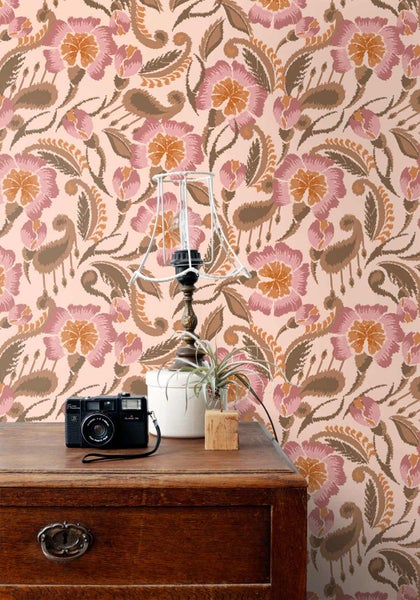 Tapete mit Vintage-Blumen- und Paisley-Muster an einer Wand hinter einer Holzkommode mit Lampe und Kamera.