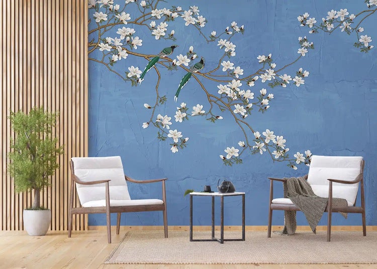 Wohnzimmer mit Fototapete, blühender Ast mit weißen Blüten und zwei Vögeln auf blauem Hintergrund, zwei Holzstühle mit weißen Polstern.