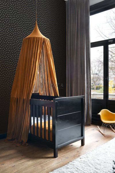 Ein Kinderzimmer mit einem schwarzen Gitterbett und einem Moskitonetz in einem warmen Farbton