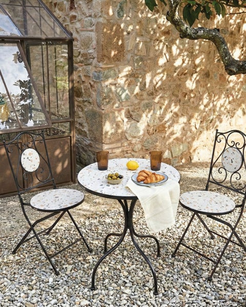 Gartenszene mit Tisch, zwei Stühlen, Speisen und Getränken auf Kies