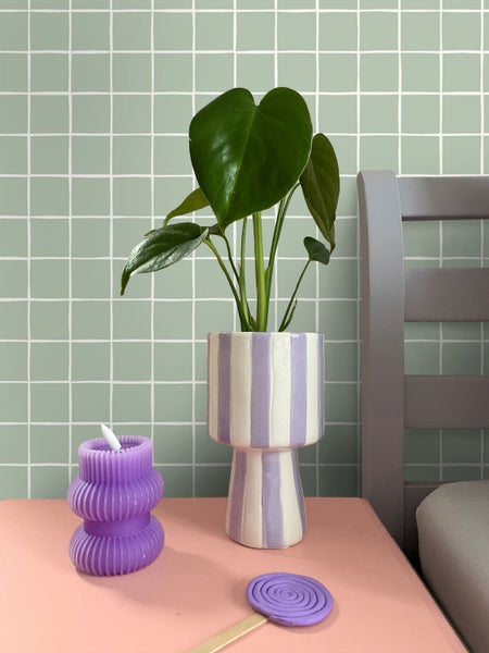 Dekorative Szene mit Kerze, Monstera Pflanze in gestreiftem Topf und Polymer Ton Lollipop