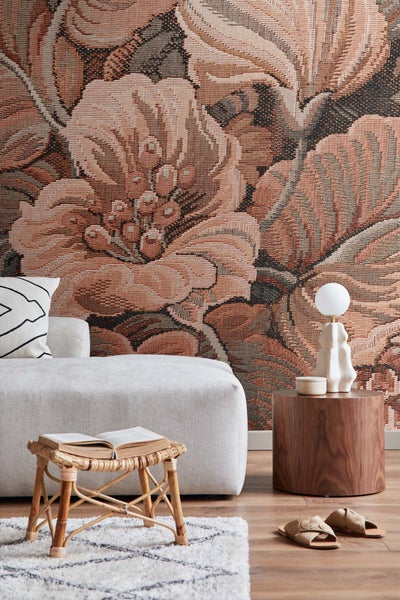 Wohnzimmer mit floraler Wandtapete, Sofa, Beistelltisch und Rattanhocker mit Buch