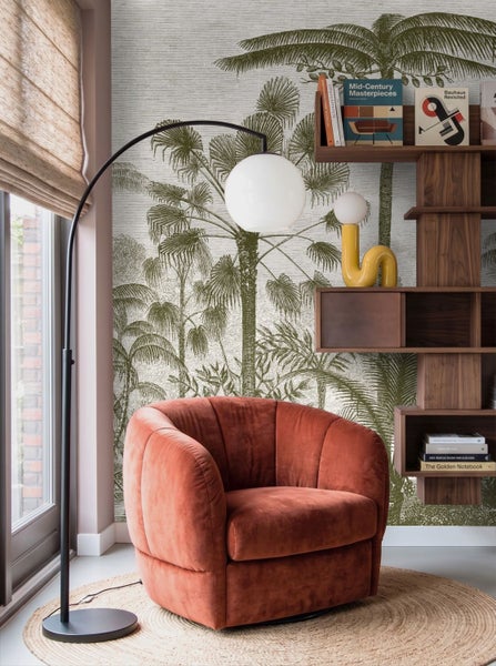 Vliestapete mit tropischem Palmenmuster in einem modern eingerichteten Wohnzimmer mit Sessel, Regal und Stehleuchte.
