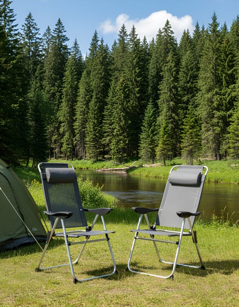 Zwei Campingstühle stehen auf einer Wiese am Flussufer vor einem Zelt.
