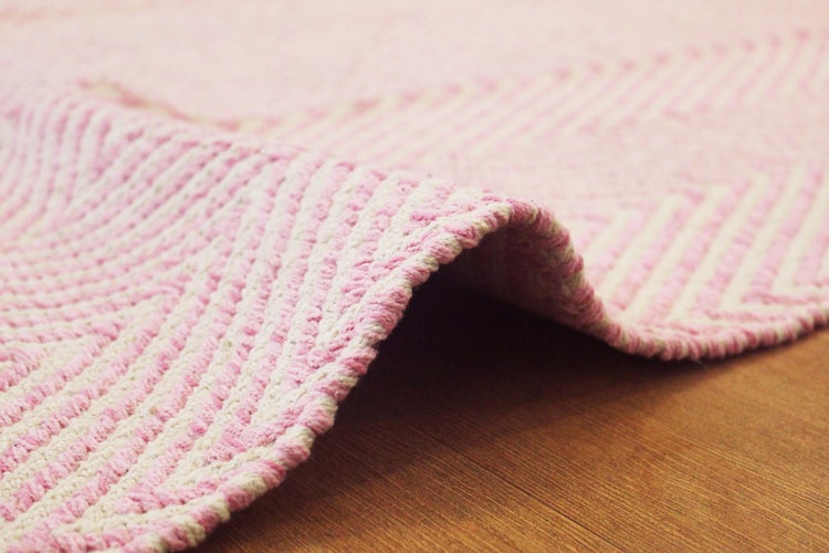Gewebter Teppich in Rosa und Weiß mit Zickzack-Muster, Nahaufnahme mit umgeklappter Ecke, texturierte Oberfläche.