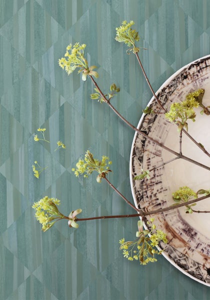 Dekoratives Stillleben mit gemusterter Tapete, Ästen und einer Schale