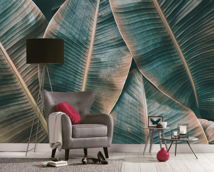 Fototapete mit großen Bananenblättern in einem modern eingerichteten Wohnzimmer mit grauem Sessel und Stehlampe.