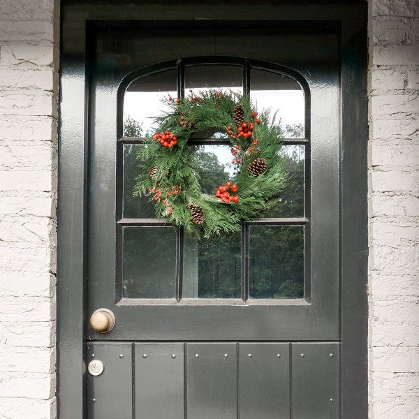 Dekorativer Weihnachtskranz mit Tannenzweigen, roten Beeren und Zapfen an einer Haustür.