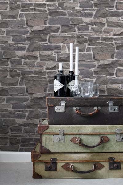 Dekorative Szene mit gestapelten Vintage-Koffern, Getränkeflaschen, Kerzen und Mauerwerk-Tapete