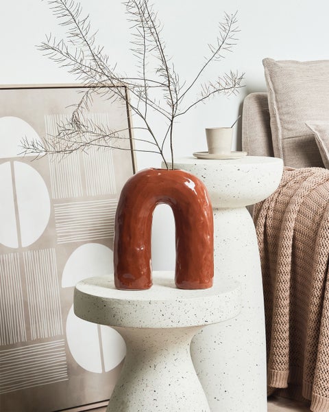 Dekorative Szene mit einer U-förmigen Vase auf einem Beistelltisch, ergänzt durch Kunst und Textilien