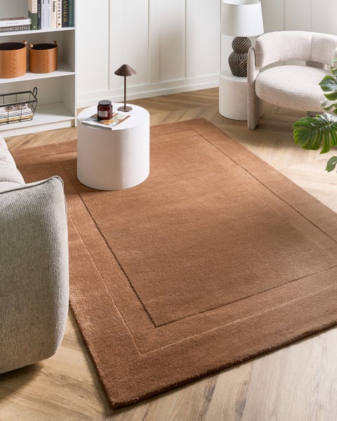 Moderner, rechteckiger Kurzflor-Teppich in Braun mit dekorativer Bordüre in einem hellen Wohnzimmer auf Fischgrät-Parkett.