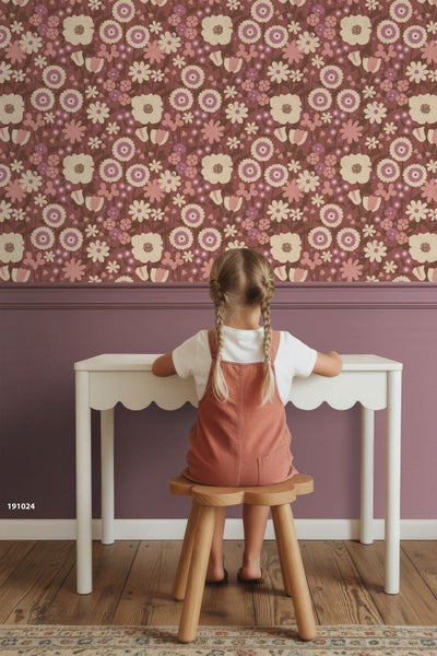 Kind sitzt an einem weißen Schreibtisch in einem Zimmer mit floraler Tapete und einem hölzernen Hocker in Blumenform.