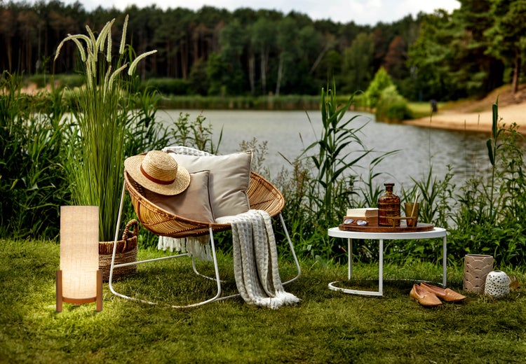 Szene mit Korbsessel, Tisch, Lampe und dekorativen Elementen im Garten