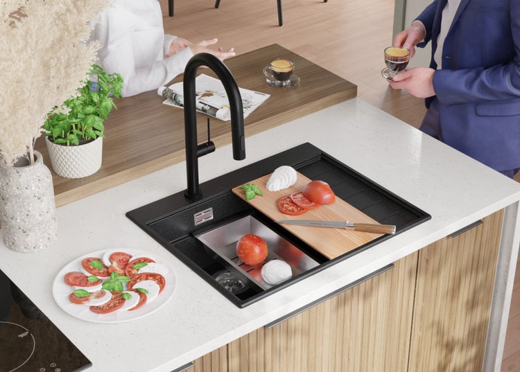 Küchenspüle mit Armatur, Schneidebrett mit Tomaten und Mozzarella, Zubereitung von Speisen in einer hellen Küche.