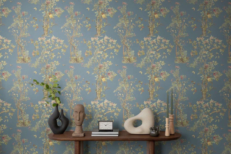 Vliestapete mit floralem Baum- und Blumenmuster vor einem Konsolentisch mit dekorativen Wohnaccessoires.
