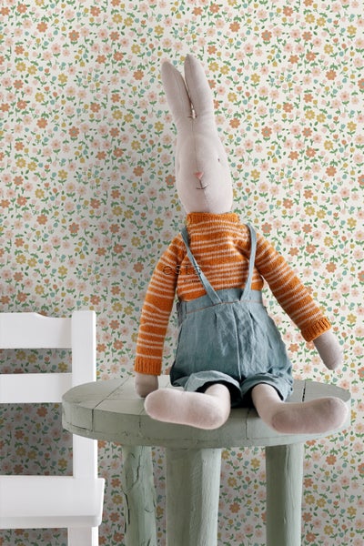 Dekorative Szene mit Stofftierhase auf einem kleinen Tisch vor einer Blumentapete.