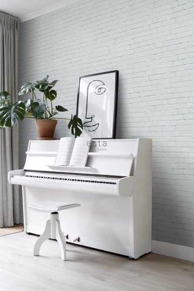 Wohnraum mit weißem Klavier, Klavierhocker, Zimmerpflanze und einer Wand mit Backsteintapete.