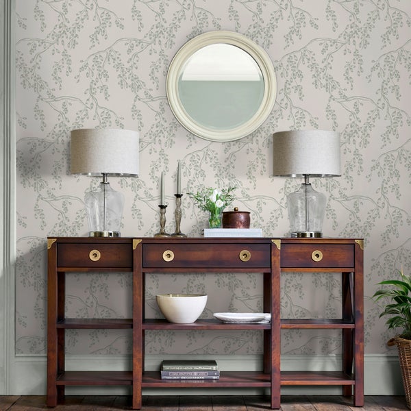 Organisiertes Zimmer mit Tapete mit Blattmuster, einem Sideboard aus dunklem Holz, einem runden Spiegel und zwei Tischlampen.