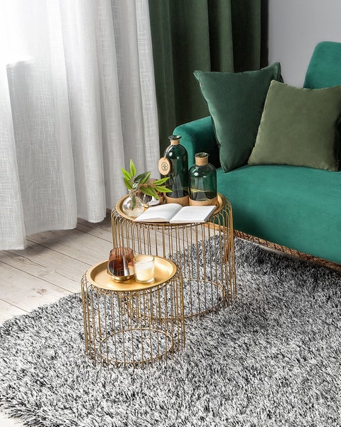 Wohnzimmerdekoration mit goldenen Beistelltischen, Glasvasen und einem grünen Sofa.