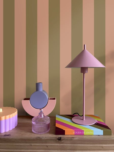 Tapete mit vertikalen Streifen in Terrakotta und Olivgrün hinter einer Kommode mit Tischlampe und verschiedenen Dekorationsobjekten.