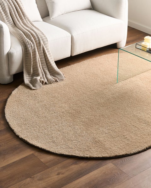 Beigefarbener runder Hochflor-Teppich in einem hellen Wohnzimmer vor einem Sofa auf Holzboden.