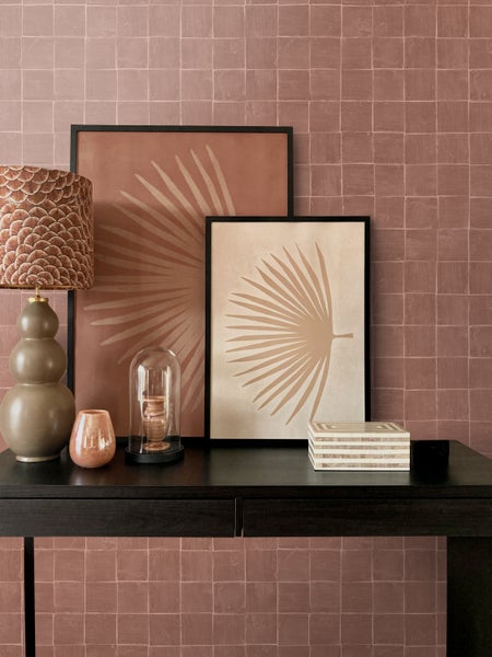 Einrichtungsidee mit Tisch, Tischlampe, Dekoration und zwei Bildern mit Pflanzenmotiven vor einer Wand mit Fliesen.