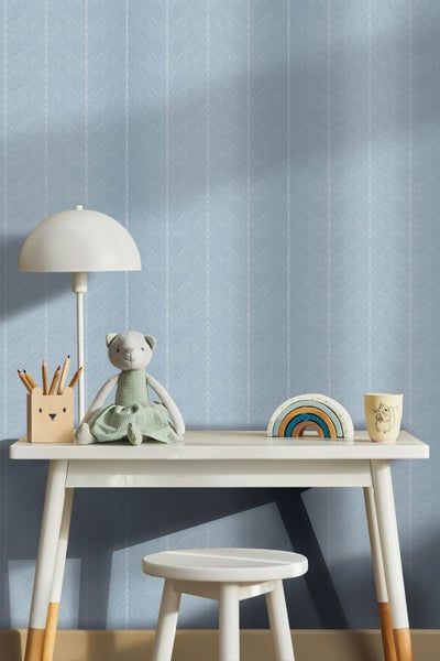 Blaue Tapete mit weißem Fischgrätenmuster an einer Wand in einem hellen, organisierten Raum hinter einem weißen Sideboard mit Kinderzimmer-Deko.