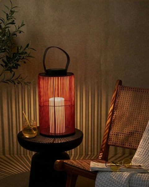 Außen-Solarleuchte aus Bambusstäben mit Tragegriff und LED-Kerze auf einem Beistelltisch neben einem Korbsessel.