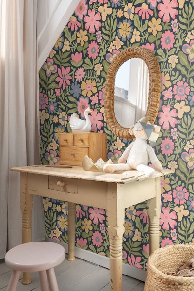 Kinderschreibtisch vor einer Wand mit Blumentapete, ovaler Korbspiegel und Stofftier.