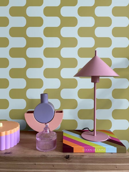 Dekorative Szene mit Lampe, Dose, Schmuckkästchen und abstrakter Kunst auf einem Tisch vor einer gemusterten Tapete