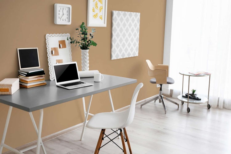 Modernes Home-Office mit grauem Schreibtisch, weißen Stühlen und hellbrauner Wand mit Dekoration. Heller und organisierter Arbeitsbereich.