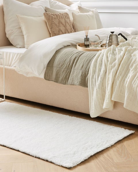 Helles Schlafzimmer mit Bett, Kissen, Tagesdecke und Teppich