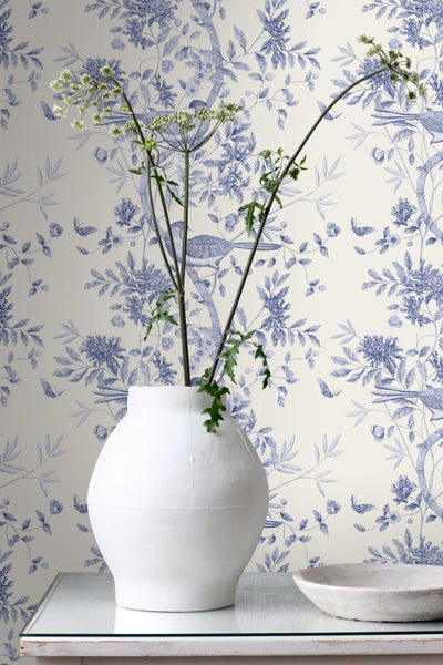 Tapete mit Toile-de-Jouy-Muster aus Blumen und Vögeln, klassische Vliestapete hinter einer dekorativen Vase auf einem Tisch.