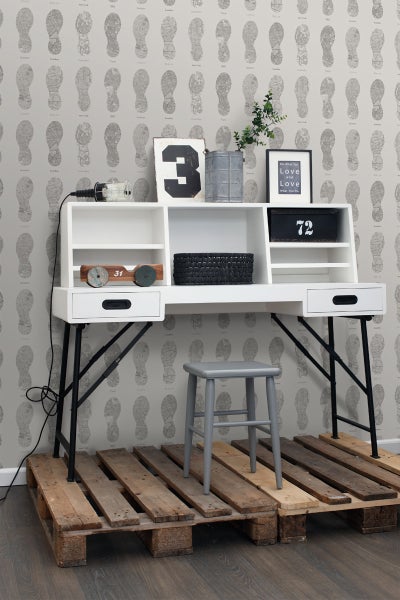 Schreibtisch mit Ablagefächern, Metallbeinen und Hocker auf Holzpaletten vor Tapete mit Fußabdruckmuster