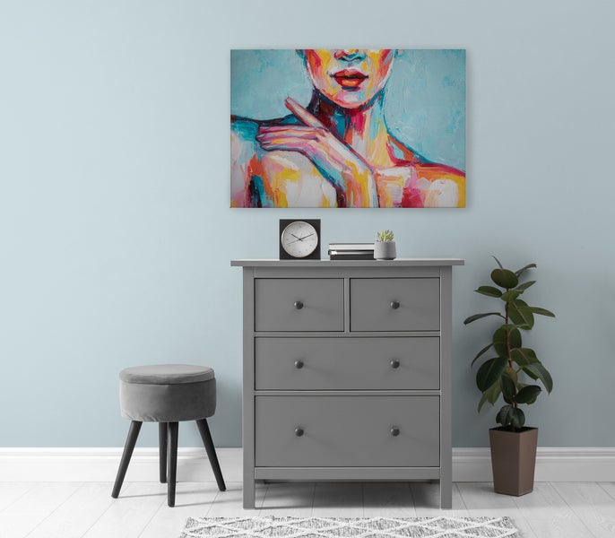 Wandbild mit abstraktem Frauenporträt über einer grauen Kommode mit Hocker und Pflanze in einem modern eingerichteten Raum.