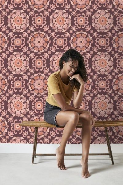 Frau sitzt vor einer Wand mit geblümter Tapete