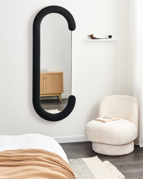 Innenraumszene mit einem Spiegel mit ungewöhnlichem Rahmen, einem Sessel, einem Schrank und einer Wandregal.