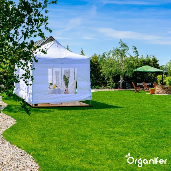 Weißes Partyzelt mit Fenstern auf einem Holzpodest in einem hellen, organisierten Garten mit Rasen und Bäumen. Organifer Logo.