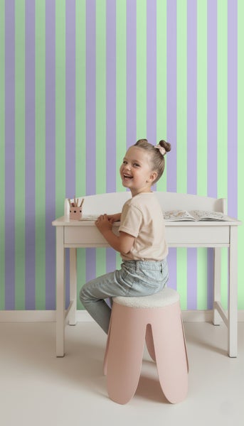 Mädchen sitzt an einem Schreibtisch vor einer gestreiften Tapete