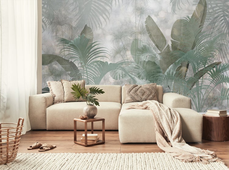 Wohnzimmer mit Sofa, Kissen, Tisch und Deko vor einer Tapete mit Pflanzenmotiven.