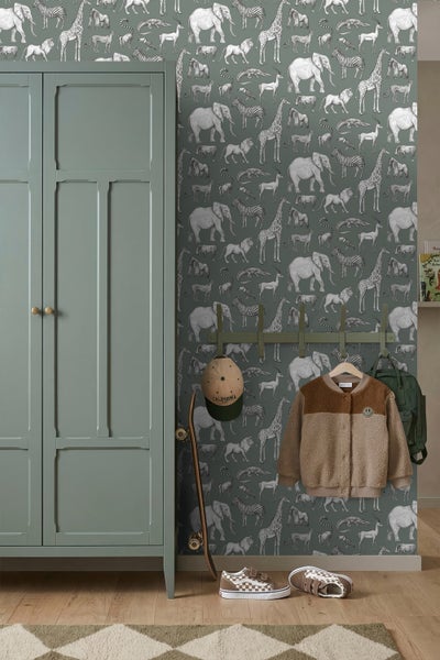 Kinderzimmer mit safari-gemusterter Tapete mit Elefanten und Giraffen, grünem Kleiderschrank, Wandhaken mit Jacke und Rucksack auf Holzboden.