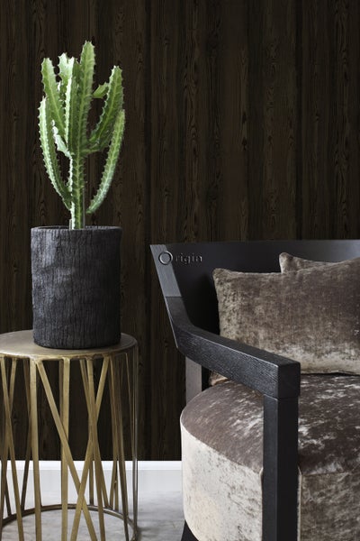 Dekorative Szene mit Kaktus in einem Topf auf einem Beistelltisch neben einem Sessel mit Kissen vor einer dunklen Holzwand