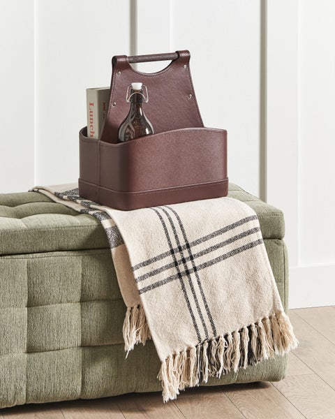 Dekorative Lederbox mit Flasche und Buch auf einer grünen Ottomane mit karierter Decke.