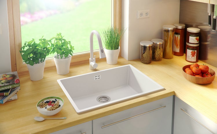 Küchenszene mit Spüle, Armatur, Kräutern im Topf und Lebensmitteln auf der Arbeitsplatte.