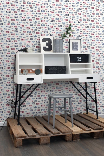 Schreibtisch mit Regalen, Schubladen und einem Hocker auf einer Holzpalette vor einer gemusterten Tapete