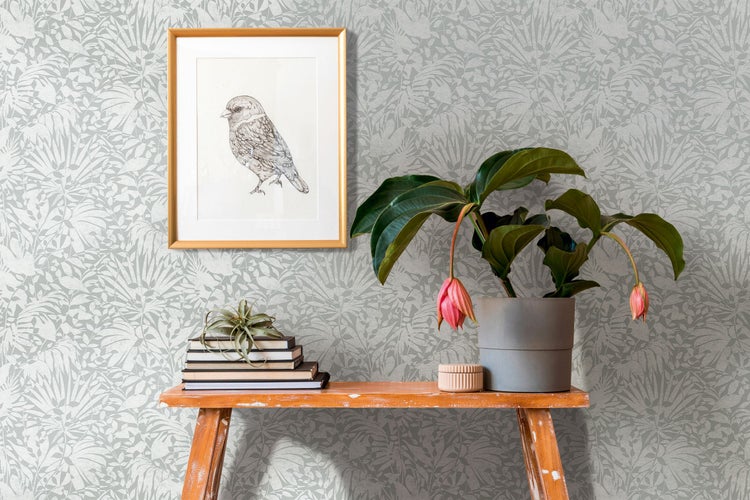 Dekoratives Interieur mit gemusterter Tapete, Vogelbild, Büchern und Zimmerpflanze auf einem Holztisch