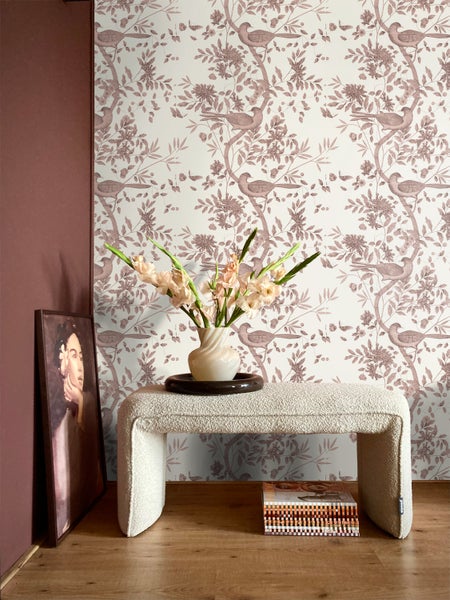 Tapete mit Vogel- und Blumenmuster in einem modern eingerichteten Raum mit einer Bouclé-Bank, einer Vase und einem gerahmten Porträt.