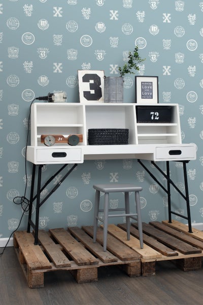 Schreibtisch mit Aufbewahrung, Hocker und Holzpaletten vor einer gemusterten Tapete